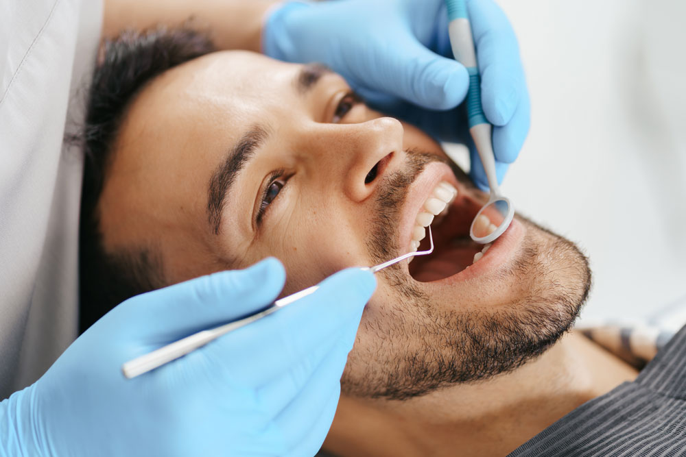lächelnder-junger-mann-sitzt-auf-zahnarztstuhl-während-arzt-seine-zähne-untersucht